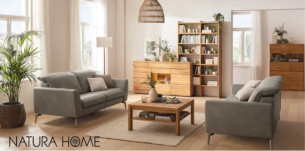 Modernes Wohnzimmer mit zwei grauen Sofas, Couchtisch und Massivholzmöbeln von NATURA HOME. Helle Einrichtung mit Regal, Sideboard und Vitrine aus Holz, kombiniert mit Pflanzen und Wohnaccessoires für natürliches Wohnen.